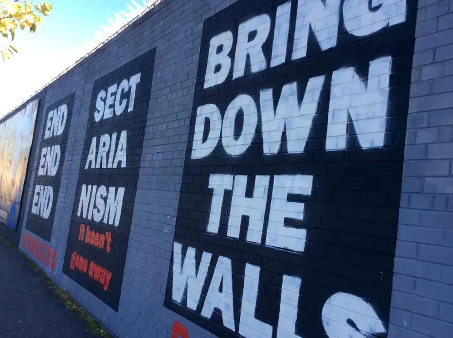 A mural reading 'End Sectarianism: Bring Down The Walls' on the Falls Road mural wall in Belfast. Image by Julia Canney. Northern Ireland, 2018. A mural reading 'End Sectarianism: Bring Down The Walls' on the Falls Road mural wall in Belfast. Image by Julia Canney. Northern Ireland, 2018.