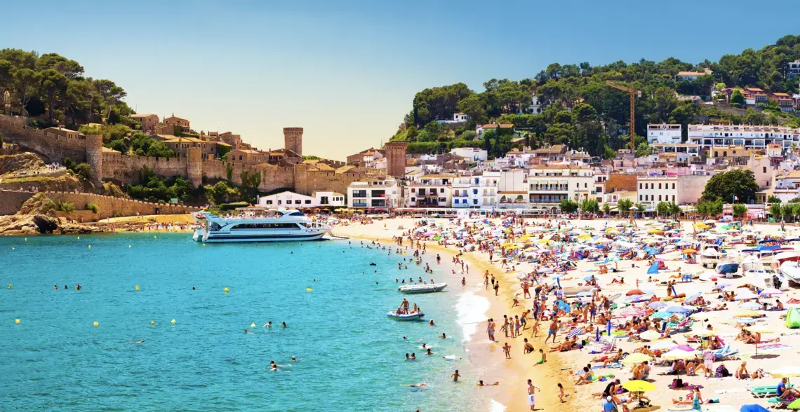 Coast with tanning and bathing people (Panorama of Costa Brava, Tossa de Mar city, Spain). Image by Denis Mironov/Shutterstock. Spain, undated. Coast with tanning and bathing people (Panorama of Costa Brava, Tossa de Mar city, Spain). Image by Denis Mironov/Shutterstock. Spain, undated.