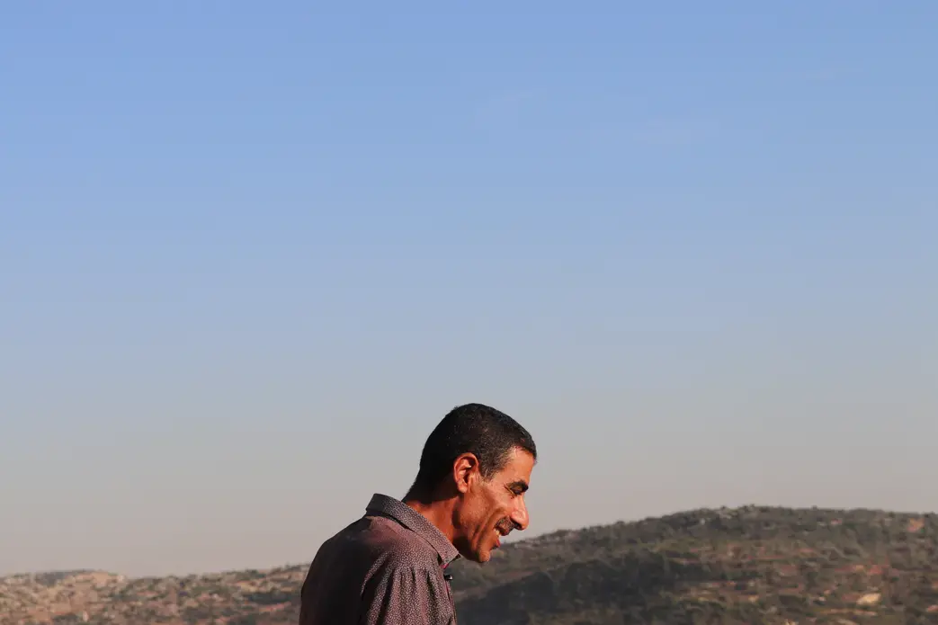 A farmer in Burqin, an agricultural village in the West Bank, stands on what's left of his olive groves. In January 2019, he received an order from the Israeli Civil Administration to uproot half his trees. A few weeks later, the remainder were razed. Image by Carly Graf. West Bank, 2019. A farmer in Burqin, an agricultural village in the West Bank, stands on what's left of his olive groves. In January 2019, he received an order from the Israeli Civil Administration to uproot half his trees. A few weeks later, the remainder were razed. Image by Carly Graf. West Bank, 2019.