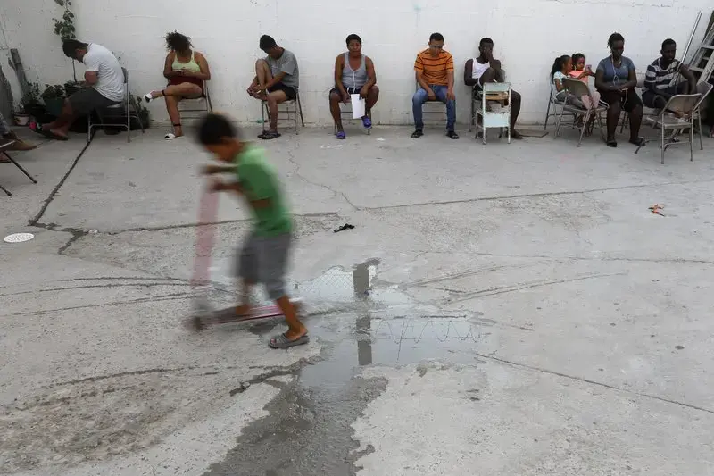 In this July 26, 2019, photo, people from Africa and Central America sit in chairs as the sun sets at El Buen Pastor shelter for migrants in Cuidad Juarez. Image by Gregory Bull. Mexico, 2019.
