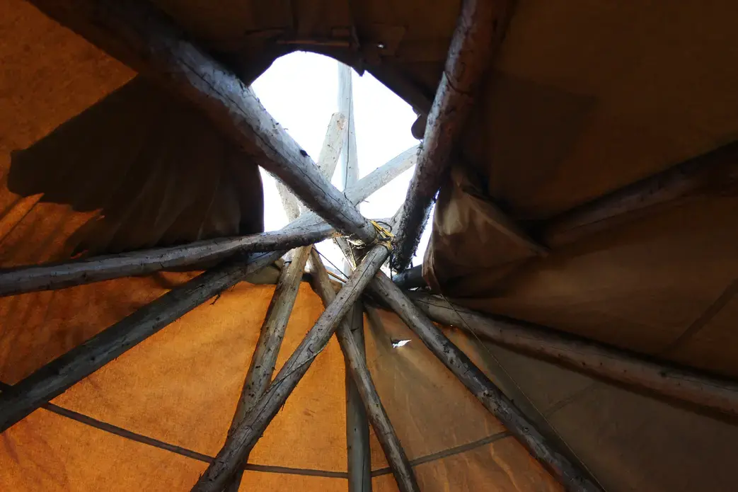 The apex of a tipi is a cluster of timber poles fastened together with rope or twine. The structure is wrapped in canvas or hide. Though once a dwelling, the tipis of St. Theresa Point are often used for storytellers to share their songs and stories with young people over a sacred fire. The poles represent unity and interdependence. Image by Dillon DeWitt. Canada, 2016. St. Theresa Point tipi