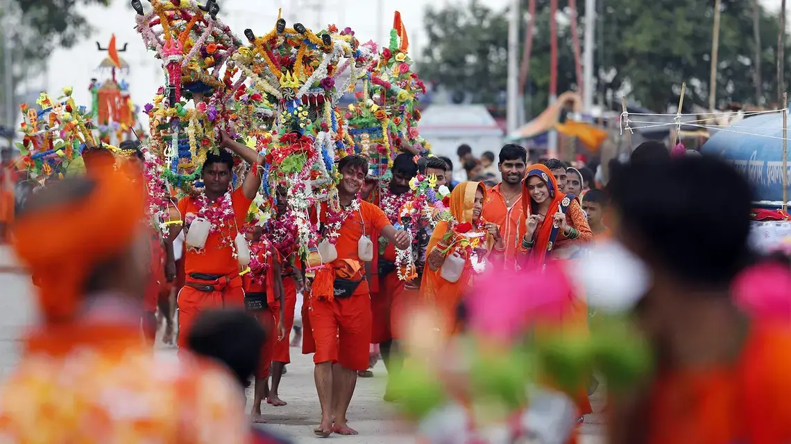 Hindu pilgrims, known as Kanwarias, walk near the banks of the Ganges River in Prayagraj, India, on July 25, 2019. Kanwarias are devotees performing a ritual pilgrimage in which they walk the roads of India, clad in saffron, and carrying ornately decorated canisters of sacred water from the Ganges River over their shoulders to take back to Hindu temples in their hometowns, during the Hindu lunar month of Shravana. Image by Rajesh Kumar. India, 2019. Hindu pilgrims, known as Kanwarias, walk near the banks of the Ganges River in Prayagraj, India, on July 25, 2019. Kanwarias are devotees performing a ritual pilgrimage in which they walk the roads of India, clad in saffron, and carrying ornately decorated canisters of sacred water from the Ganges River over their shoulders to take back to Hindu temples in their hometowns, during the Hindu lunar month of Shravana. Image by Rajesh Kumar. India, 2019.