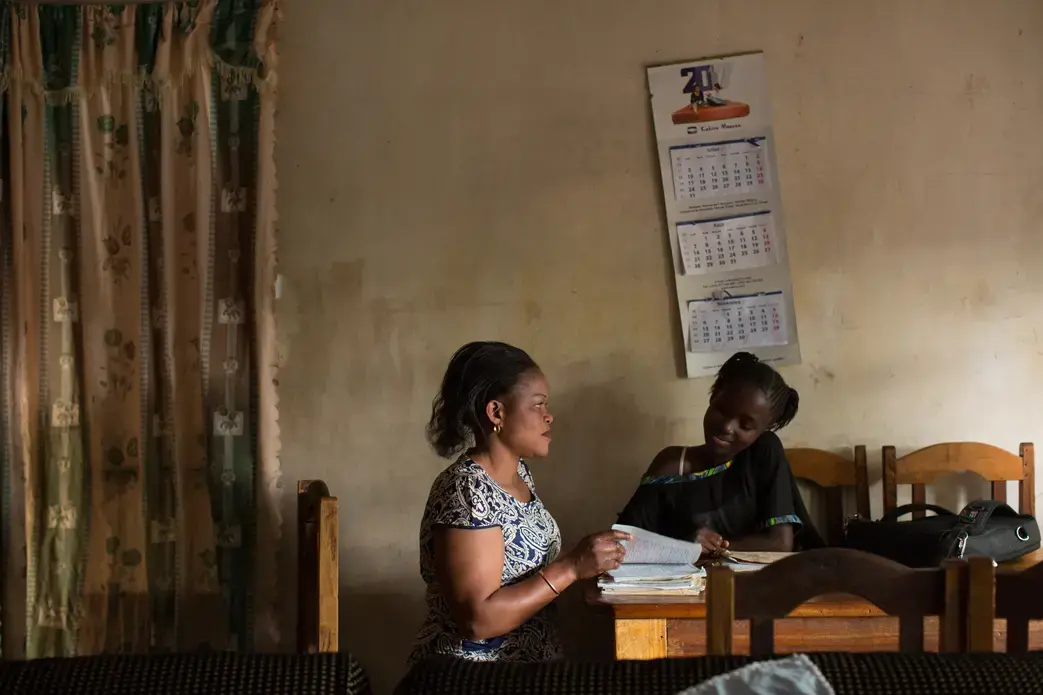FARDC captain Fanni Katora, 34, looks over the school work of her daughter Syntiche, 10, after work at their home in Goma, D.R. Congo, November 29, 2017. Image by Allison Shelley. Democratic Republic of Congo, 2017. FARDC captain Fanni Katora, 34, looks over the school work of her daughter Syntiche, 10, after work at their home in Goma, D.R. Congo, November 29, 2017. Image by Allison Shelley. Democratic Republic of Congo, 2017.