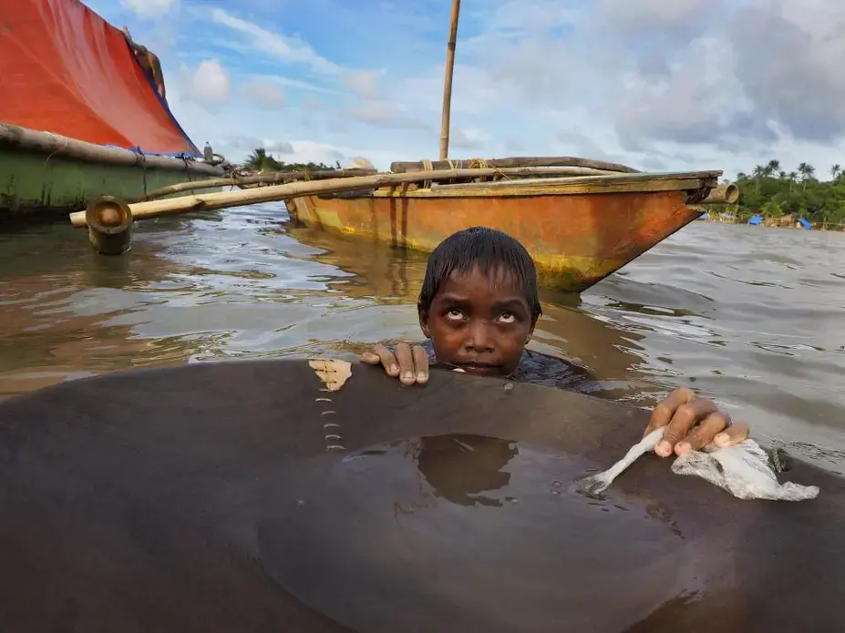Jonathon Ramorez, 12, stands waist-deep in the bay with a wooden pan he uses to separate gold from sediment. He will spend hours in the water, which often is tainted with animal waste and teeming with bacteria. Image by Larry C. Price. Philippines, 2013. Media file: 2013_price_compressormining_002.jpg