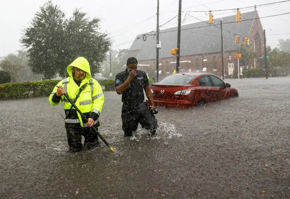 Charleston firefighter Viktor Kruzhinsky (left) uses a roof hook as a depth gauge to sound the ground in front of him while rescuing motorists trapped by floodwaters at the intersection of King and Huger streets after an intense downpour in downtown Charleston on Friday, September 25. Image by Andrew J. Whitaker / Post and Courier. United States, 2020.