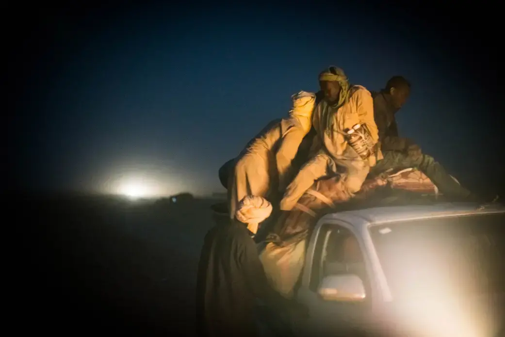 Migrants pile onto the back of a pickup truck bound for Libya on the outskirts of Agadez, Niger. The trip across the Sahara, where temperatures can soar above 120 degrees Fahrenheit, typically takes around three days. Image by Nichole Sobecki. Niger, 2017. Migrants pile onto the back of a pickup truck bound for Libya on the outskirts of Agadez, Niger. The trip across the Sahara, where temperatures can soar above 120 degrees Fahrenheit, typically takes around three days. Image by Nichole Sobecki. Niger, 2017.