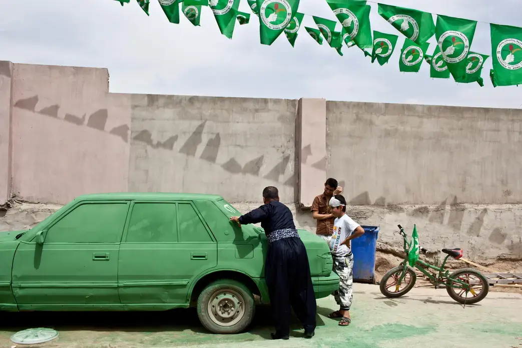 A supporter of the Patriotic Union of Kurdistan (PUK), a Kurdish political party headed by Jalal Talabani, paints slogans on a car which was painted green, the color of the party. Image by Sebastian Meyer. Iraq, 2014. Media file: sebastian_meyer_kirkuk_elections_02.jpg
