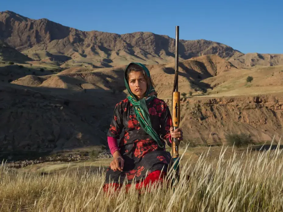 In Khuzestan Province, Masoumeh Ahmadi, 14, holds her mother’s shotgun. After a woman marries, she receives a firearm—with the approval of her husband and her father. Many women get one as a gift from their husbands after giving birth to their first son. Image by Newsha Tavakolian. Iran, 2018. In Khuzestan Province, Masoumeh Ahmadi, 14, holds her mother’s shotgun. After a woman marries, she receives a firearm—with the approval of her husband and her father. Many women get one as a gift from their husbands after giving birth to their first son. Image by Newsha Tavakolian. Iran, 2018.