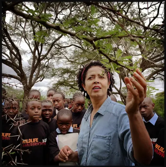 Science Leader, Kenya: CEO, conservationist, advocate: Paula Kahumbu runs the Kenyan conservation group WildlifeDirect. Kahumbu describes to city teenagers visiting Nairobi National Park the interplay between species: how ants help a native acacia tree defend itself against herbivores such as giraffes and rhinos. Image by Lynn Johnson. Kenya, 2019. Science Leader, Kenya: CEO, conservationist, advocate: Paula Kahumbu runs the Kenyan conservation group WildlifeDirect. Kahumbu describes to city teenagers visiting Nairobi National Park the interplay between species: how ants help a native acacia tree defend itself against herbivores such as giraffes and rhinos. Image by Lynn Johnson. Kenya, 2019.