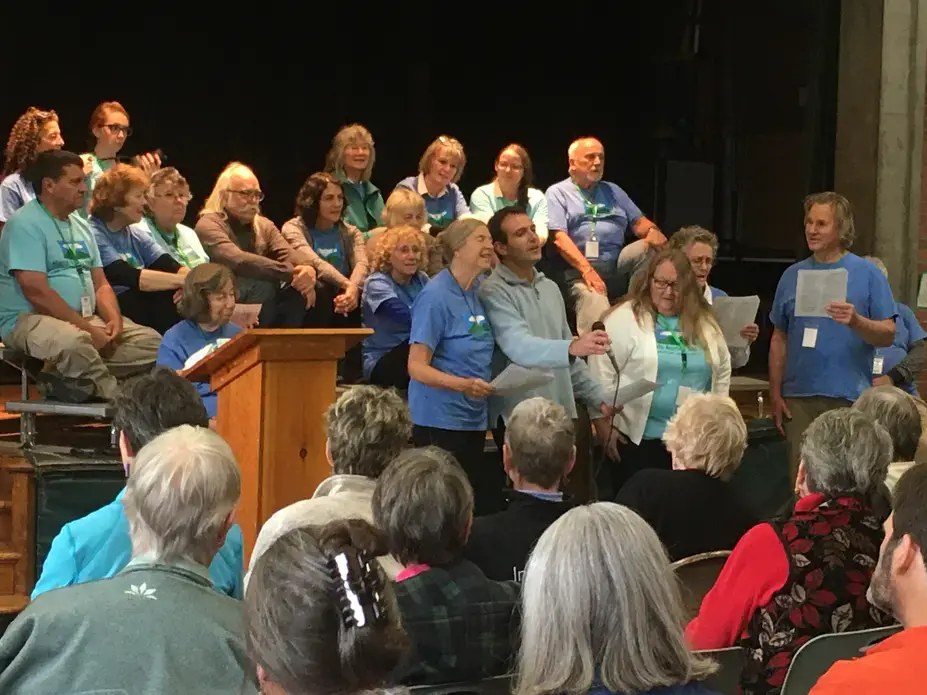 Hands Across the Hills participants sing at public forum in Leverett Elementary School’s auditorium as other group members from Kentucky and Leverett look on. Image by Richie Davis. United States, 2019.