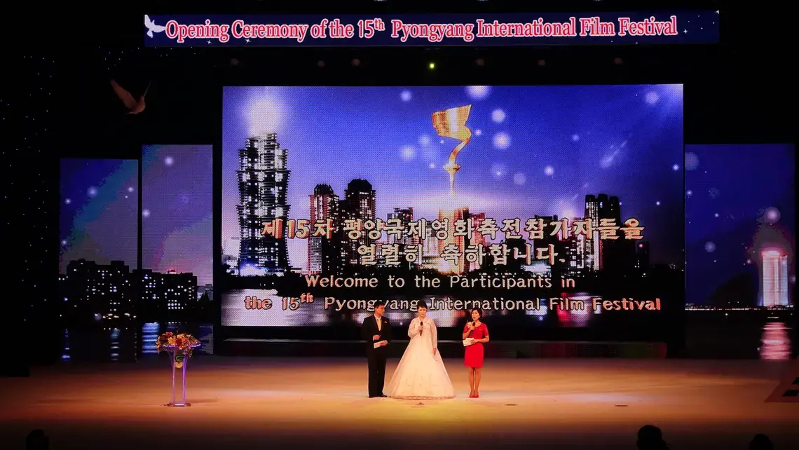 The three hosts on stage during the opening ceremony of the 15th Pyongyang International Film Festival. A sculpted dove in the top left signifies the festival's mission of peace. Image by Laya Maheshwari. North Korea, 2016. The three hosts on stage during the opening ceremony of the 15th Pyongyang International Film Festival. A sculpted dove in the top left signifies the festival's mission of peace. Image by Laya Maheshwari. North Korea, 2016.