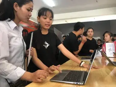Young women attending the BarCamp ASEAN 2018 expo in Phnom Penh test the KOOMPI laptop. Image from Facebook/KOOMPI. Cambodia, 2018. Young women attending the BarCamp ASEAN 2018 expo in Phnom Penh test the KOOMPI laptop. Image from Facebook/KOOMPI. Cambodia, 2018.