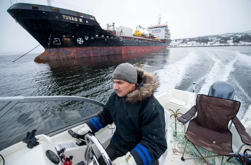 Karl Michelin speeds past a fuel tanker docked at the Rigolet dock for one of two yearly fuel drops on November 10, 2019. Image by Michael G. Seamans. Canada, 2019. Karl Michelin speeds past a fuel tanker docked at the Rigolet dock for one of two yearly fuel drops on November 10, 2019. Image by Michael G. Seamans. Canada, 2019.