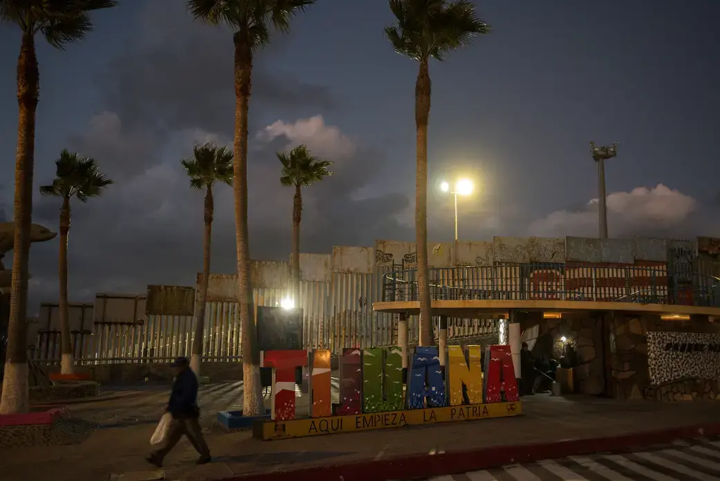 A man strolls past a Tijuana sign popular with tourists near the border wall at dusk in Playas de Tijuana on Nov. 29. Image by Amanda Cowan. Mexico, 2019.