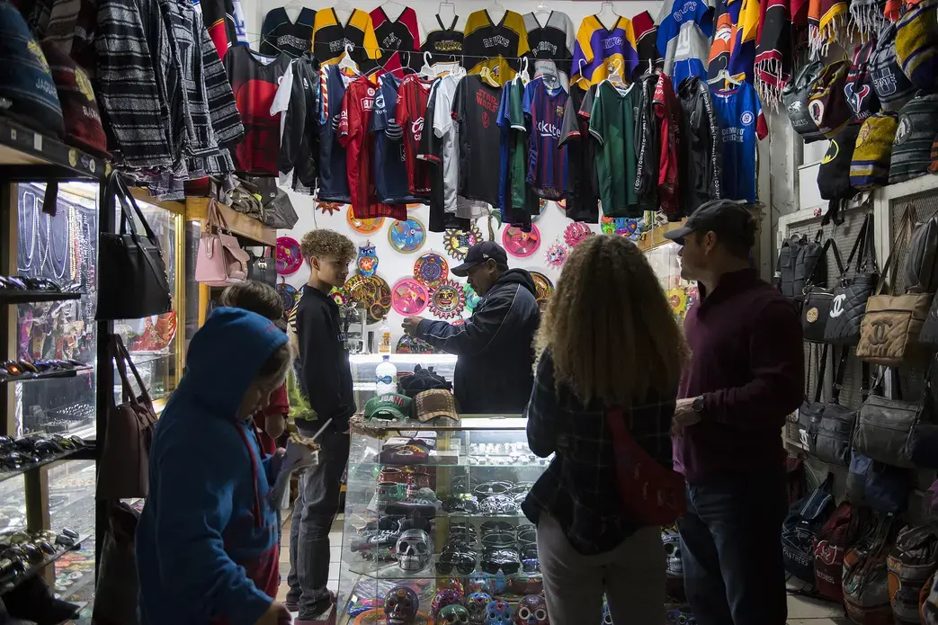 Raymond Flores looks to his father, Ramon, right, for approval as he shops for his birthday present with his siblings along Avenida Revolucion in Tijuana, Mexico. The chain costs 750 pesos, which is approximately $38. Ramon, who makes around $110 a week, said he wanted him to have the gift. 'When I get the opportunity to give them something they want, I feel good,' he said. Image by Amanda Cowan. Mexico, 2019.