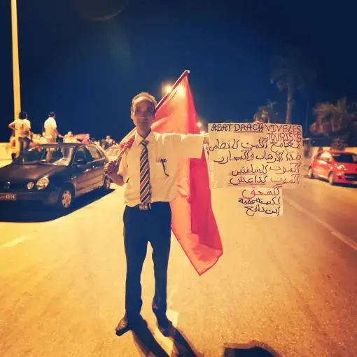 At a protest the evening following a mass beach shooting attack, a Tunisian man in Sousse holds up a banner in French and Arabic condemning ISIL and showing solidarity with the foreign tourists who were targeted. Image by Alice Su. Tunisia, 2015.