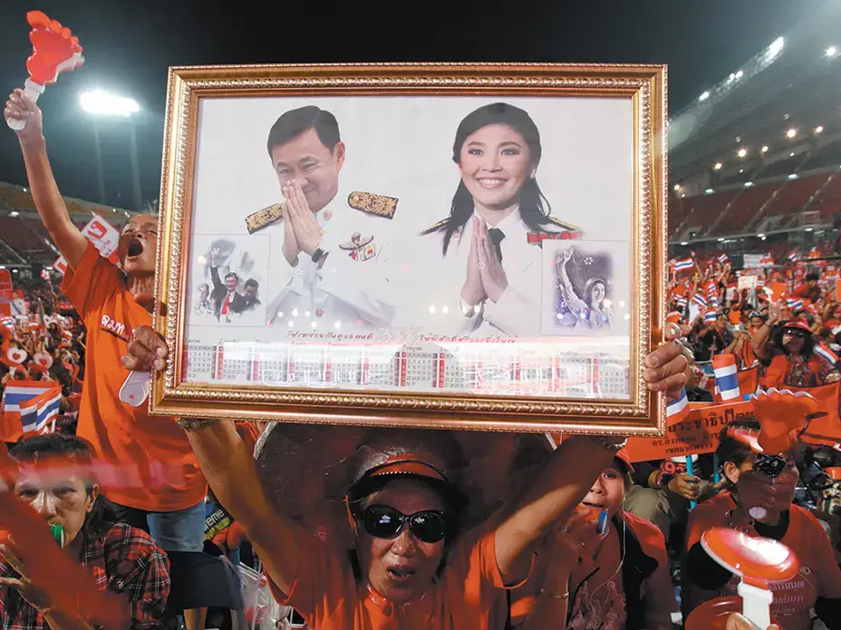 A Red Shirt supporter holding pictures of Thailand’s ousted prime minister Yingluck Shinawatra and her brother, former prime minister Thaksin Shinawatra, at a rally in Bangkok. Image by Kerek Wongsa. Thailand, 2013. Media file: thth.jpg