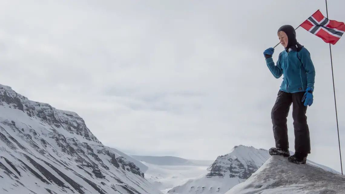 A child carries a Norwegian flag on a high Arctic landscape. Image by Amy Martin. Norway, 2018. A child carries a Norwegian flag on a high Arctic landscape. Image by Amy Martin. Norway, 2018.