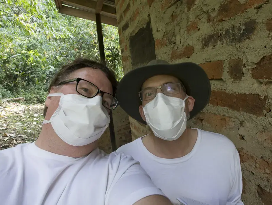 Milwaukee Journal Sentinel photojournalist Mark Hoffman (left) and reporter Mark Johnson are shown  inside Kibale National Park in Uganda. They are wearing masks while photographing and examining large bats, which are renowned for their ability to carry pathogens. Kibale Forest boasts the highest number of primate species in the world. Image by Mark Hoffman. Uganda, 2017.