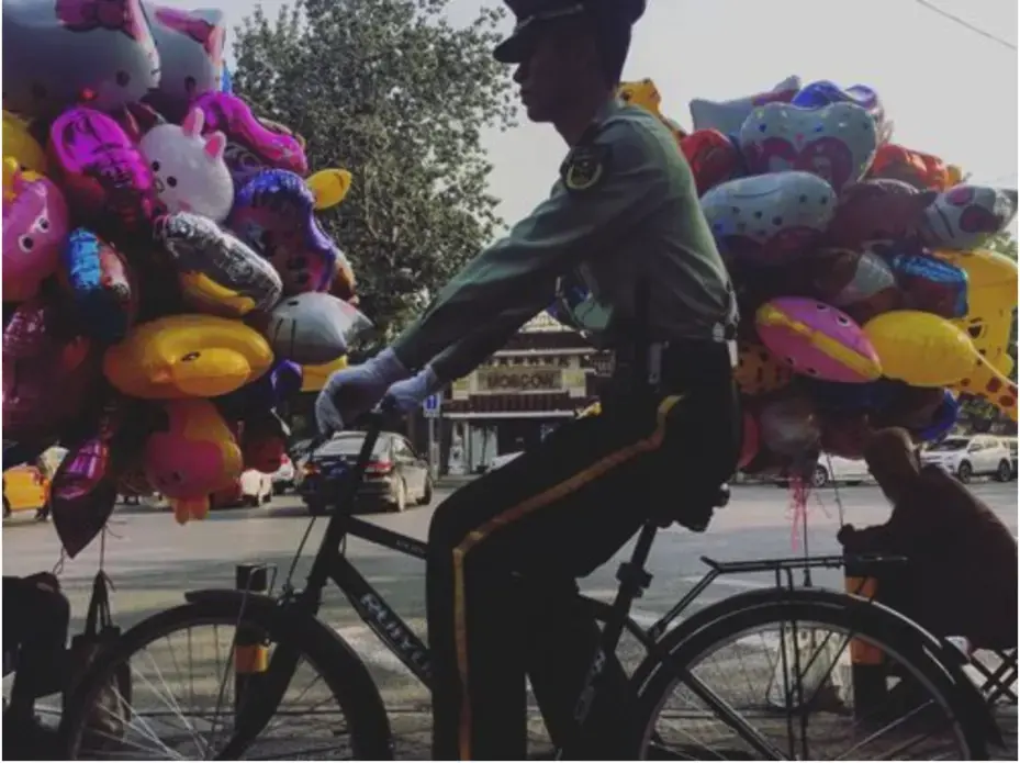 A member of the Chinese military rides his bike past two men selling balloons on Sunday, Sept. 24, 2017, on the same block as the residence of U.S. Ambassador to China Terry Branstad in Beijing, China. Image by Kelsey Kremer. China, 2017.