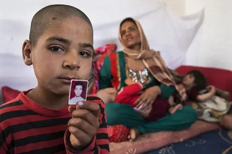 Hamid, in 2014, holds a photo of his father, who was killed during his service in the Afghan army, leaving Fereshta, at rear, widowed with five children. Image by Paula Bronstein/The Wall Street Journal. Afghanistan, 2014. Media file: bn-kk496_0915af_p_20150921183833.jpg