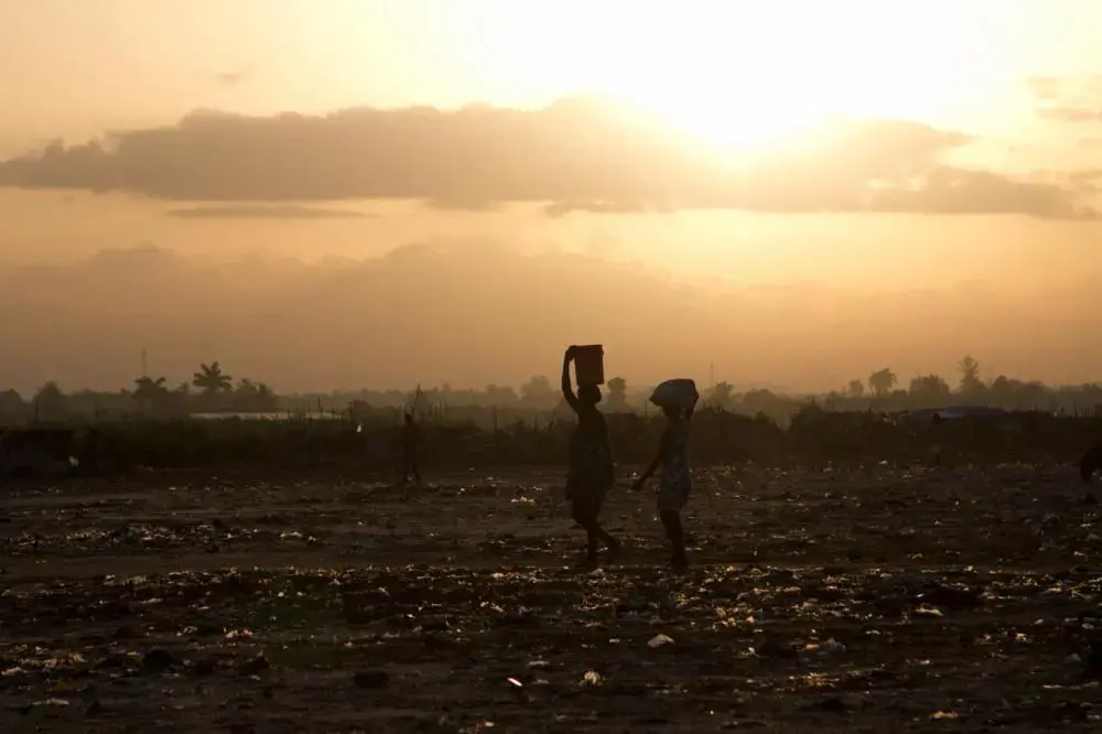 From Meghan Dhaliwal's student fellow project: Two women cross a field in Cité Soleil. They carry necessities for the day on their heads. Image by Meghan Dhaliwal. Haiti, 2012. Media file: dhaliwal-10_dark.jpg