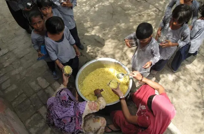 A meal of "khichdi" made with rice, lentils and some vegetables being served to primary school children at a government-run girls' school in the village of Dujanna, Haryana. Image by Rhitu Chatterjee. India, 2014. Media file: serving_kids2.jpg