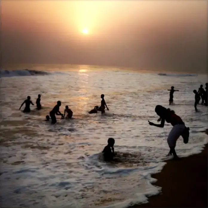 From the Everyday Africa Instagram (@everydayafrica): "A woman photographs children playing in the ocean in Grand-Bassam, Ivory Coast on Sept. 12, 2013. Just outside of Abidjan, Ivory Coast's largest city, Grand-Bassam is a popular weekend destination for thousands of Ivorians." Image by Peter DiCampo. Ivory Coast, 2013.