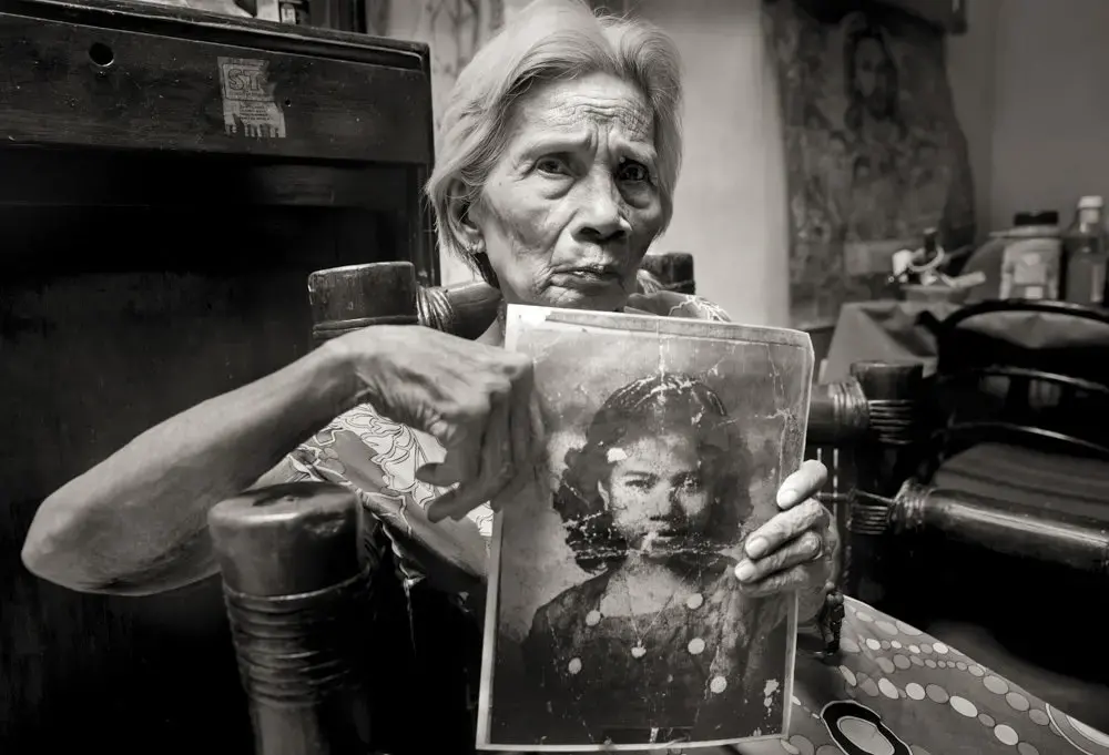 Fedencia Nacar David holds her photo for an application to work as a maid. She was 15. A year before, a Japanese soldier sliced her ear and threatened to behead her if she didn't go to a garrison with him; she was raped over 10 days. "It still hurts," she says. "I was innocent. Why did that happen to me?" She kept her past from her children until "comfort women" began speaking out in the 1990s. Image by Cheryl Diaz Meyer. Philippines, 2019.