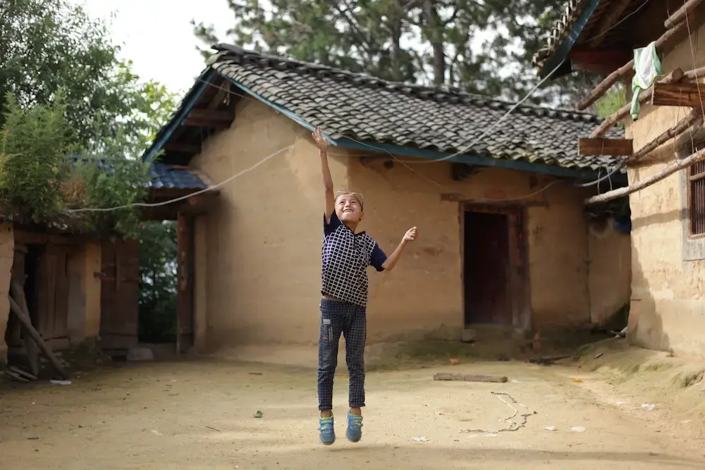 Eight-year-old Wang Jie jumps for the washing line in the courtyard of his family’s farmhouse in Liangshan Prefecture, Sichuan Province. Image by Max Duncan. China, 2016.