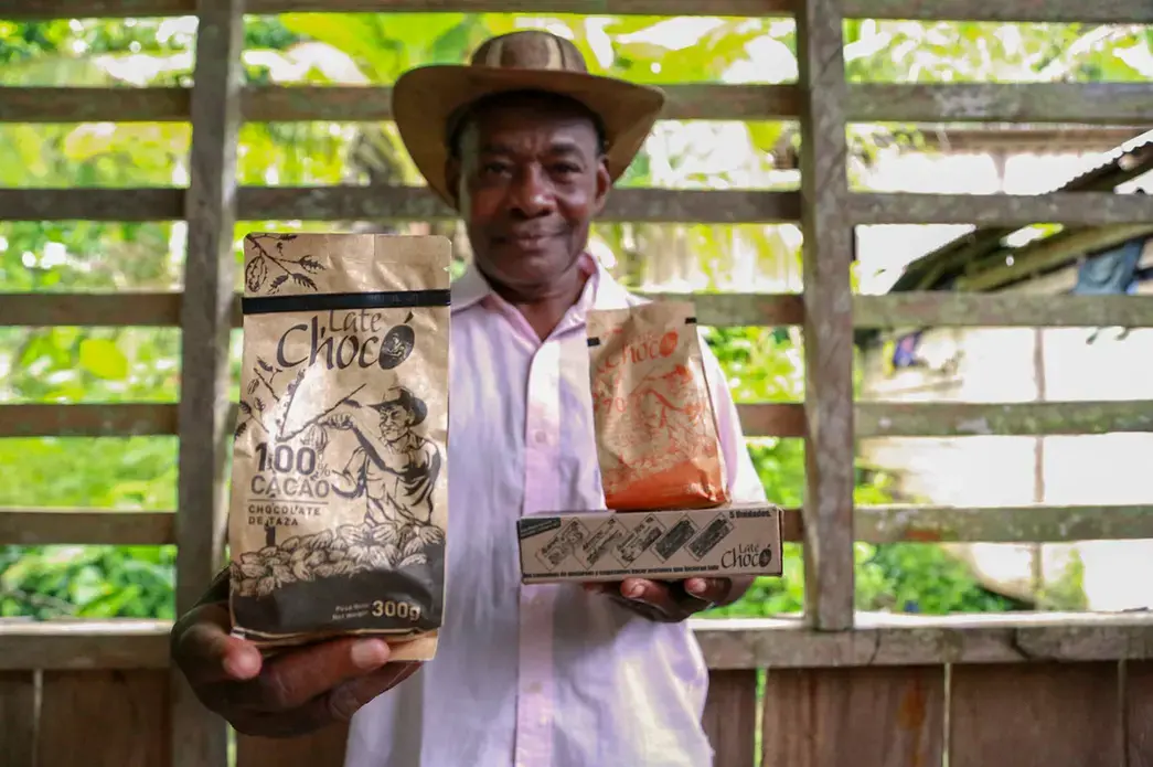 José Palacios, a cacao farmer, holds the Late Chocó chocolate products produced by his son, Joel, in Bogotá. The package bears an illustration of his likeness. José Palacios lives in Colombia's western Chocó department, which is also a coca-growing region. Image by Verónica Zaragovia. Colombia, 2018. José Palacios, a cacao farmer, holds the Late Chocó chocolate products produced by his son, Joel, in Bogotá. The package bears an illustration of his likeness. José Palacios lives in Colombia's western Chocó department, which is also a coca-growing region. Image by Verónica Zaragovia. Colombia, 2018.