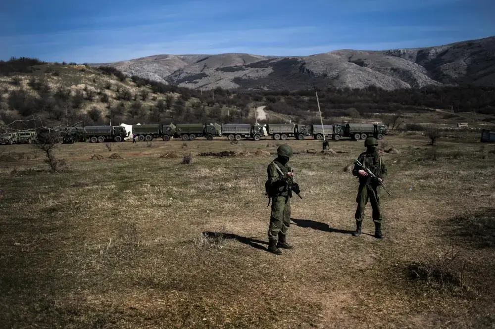 Unidentified military men, believed to be Russian servicemen, are seen in front of a convoy of military trucks, located near the base of the Ukrainian Navy's coastal guards. Image by Boryana Katsarova. Crimea, 2014. Media file: the_nation_selection_crimea_press_freedom_07.jpg