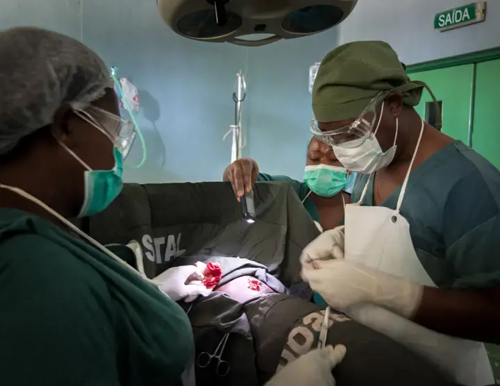 Victor Muitiquile closes a stab would by the light of a cellphone after the power went out at Chokwe District Hospital in Mozambique. Image by Bridget Huber. Mozambique, 2014. Media file: moz_lil-0248.jpg