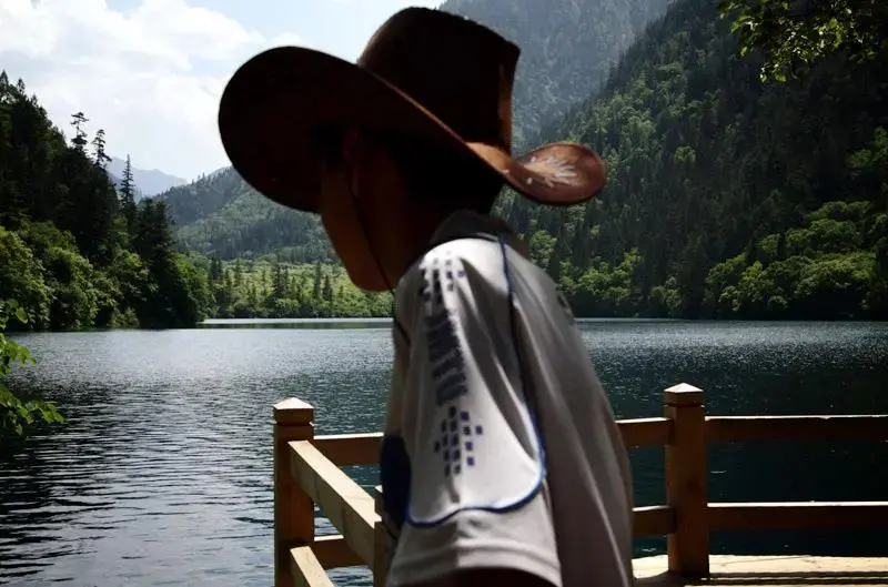 A young boy in a cowboy hat looks out onto one of the many lakes that make up the Jiuzhaigou Nature Reserve in northern Sichuan. Image by Sean Gallagher. China, 2011. Media file: 1_9921_11482.jpg