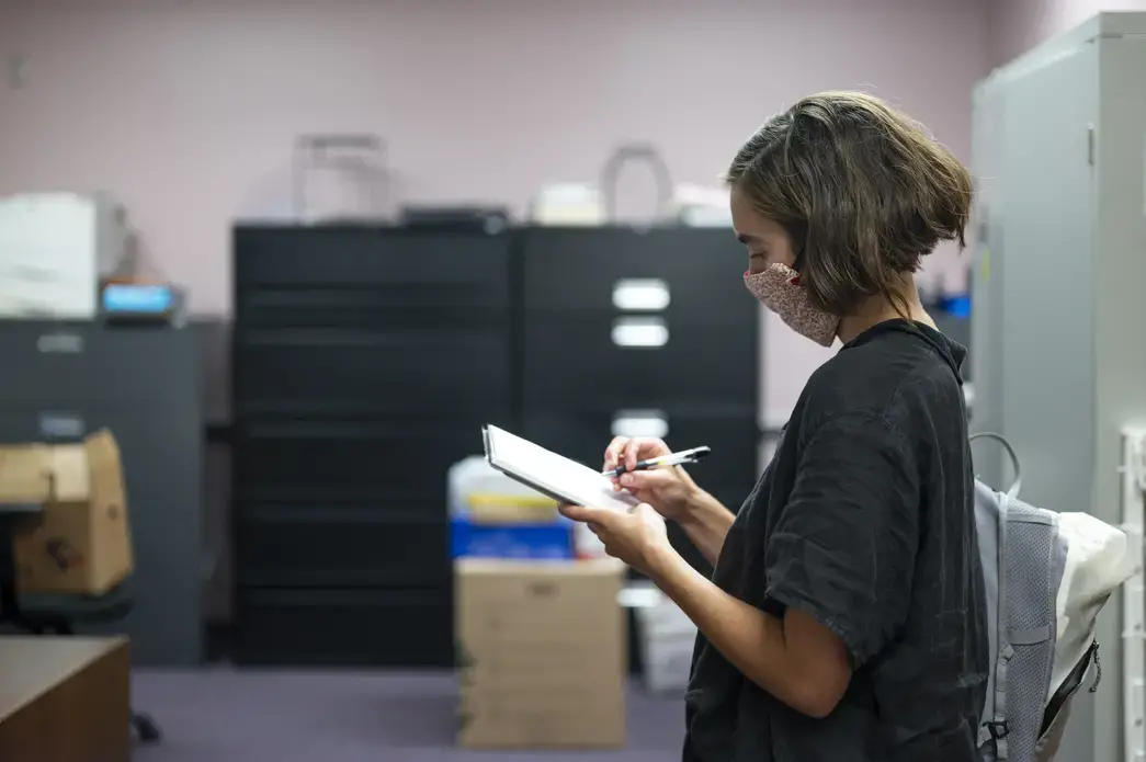 Carly Berlin, wearing a mask, stands and writes in a notebook.