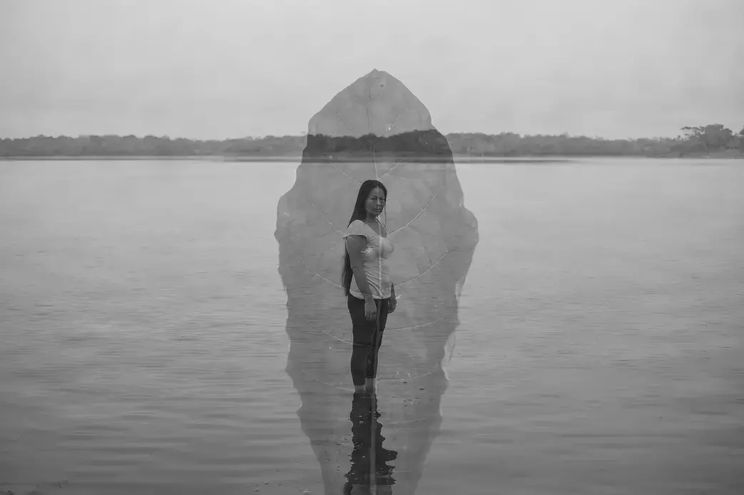 dialogoconlasplantas.jpg Black and white portrait of a woman standing in a lake, with the water coming up to her ankles. She has long dark hair and wears a white shirt and dark pants. Superimposed on top of her is a semi-translucent image of a leaf.