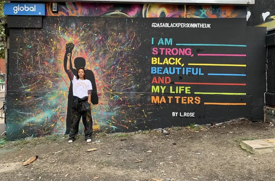 Turbo Park - Rose.jpeg A woman stands in front of a mural with her fist raised. Her pose is echoed by a figure in the mural. Text on the wall reads, "I am strong, Black, beautiful, and my life matters."
