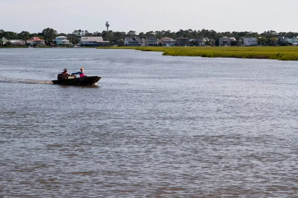 Two people ride a small boat through a lake surrounded by houses.