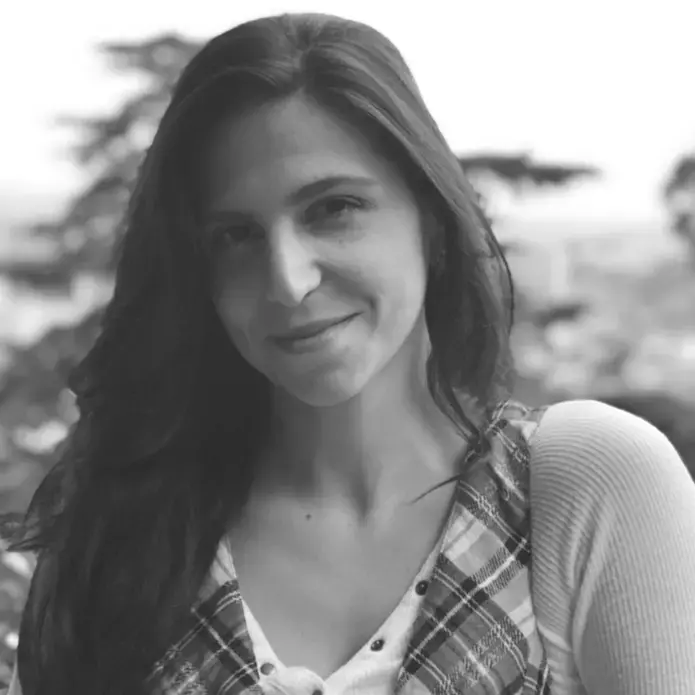 A black and white headshot of Mariana Palau, smiling at the camera wearing a plaid shirt.