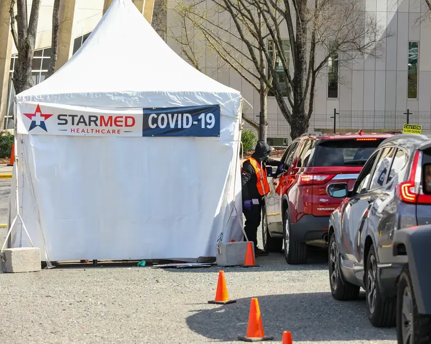 shutterstock_1940275600.jpeg Vehicles line up next to a white tent that has a banner reading, "Starmed Healthcare COVID-19."