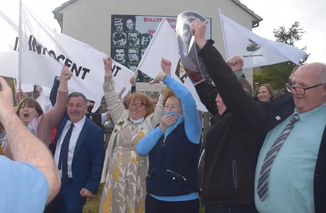 People stand and cheer in front of a building. Some hold white flags that read 'Innocent.'