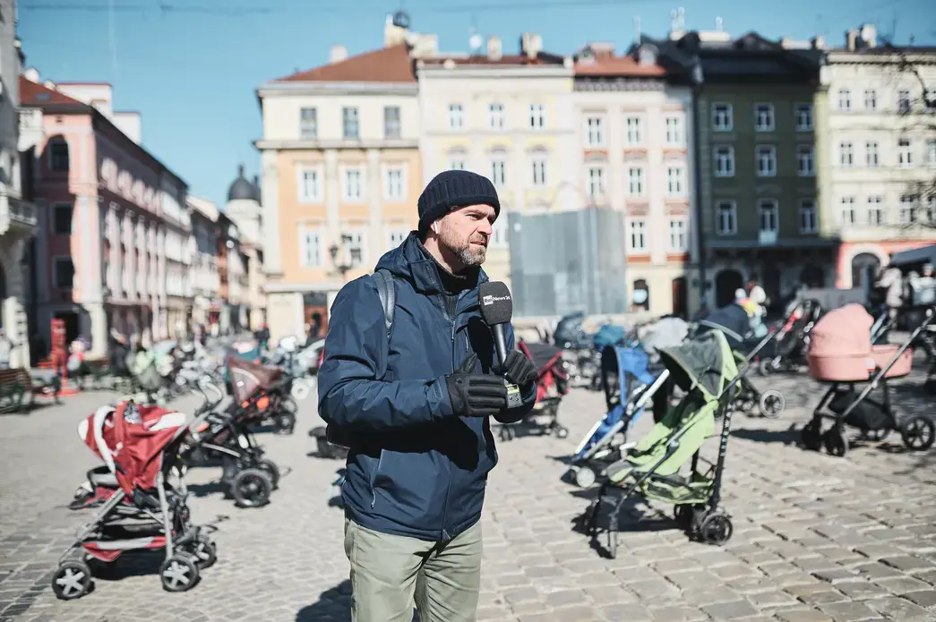 Journalist with microphone stands in a plaza filled with empty strollers