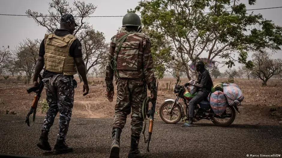Two soldiers carrying automatic rifles stop a man on a motorbike.