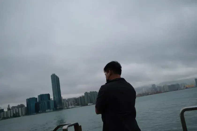 A man looks out on a city skyline bordered by water and milky sky.