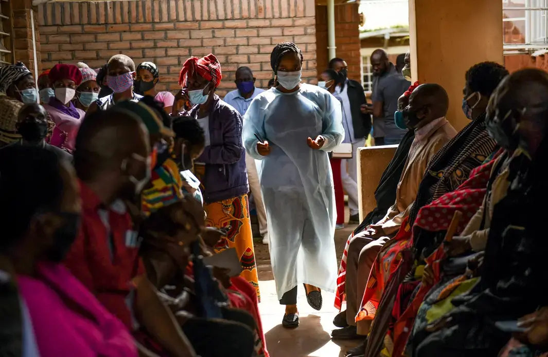 A health worker walks through a crowded clinic in Malawi. Citizens waiting for their appointments look on.