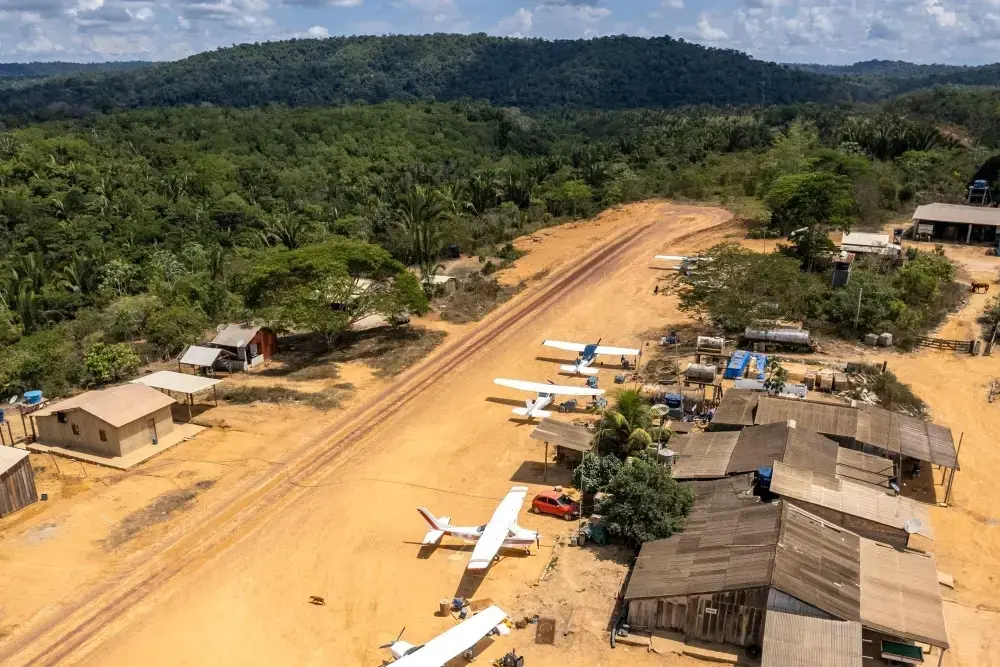 A view from above of an airstrip filled with small planes, carved out of the Amazon rainforest
