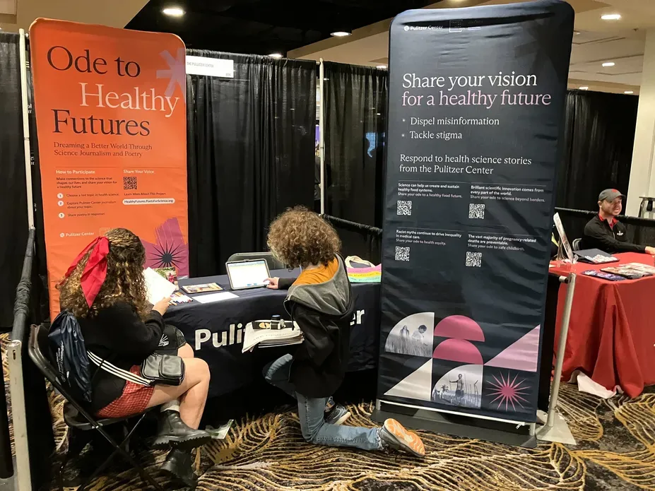 Students sit in front of a table at the JEA/NSPA trade show and write poems.
