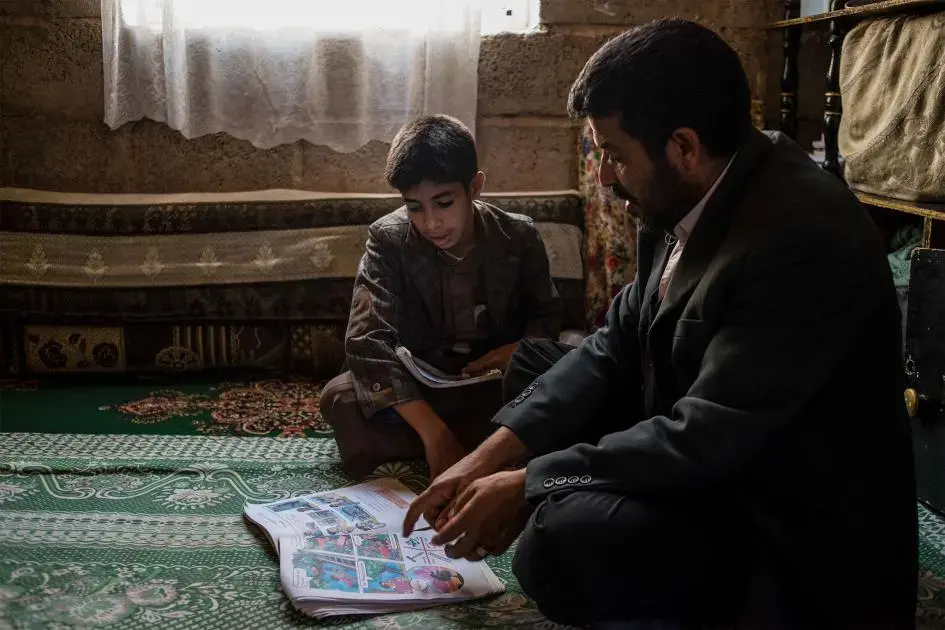Yahya reads Salah's English workbook with him, pronouncing difficult words together. Image by Alex Potter. Yemen, 2018.