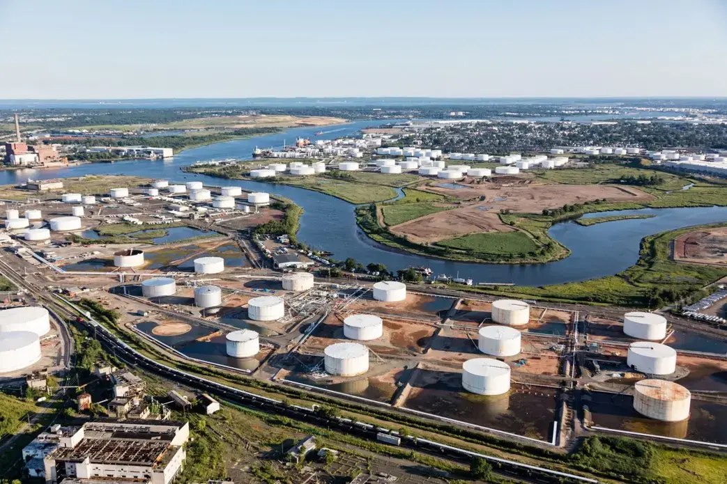 Hundreds of white petrochemical storage tanks sit on concrete pads in the wetlands near Elizabeth, New Jersey. Tanks in the foreground, owned by Kinder Morgan, store up to half a million barrels of ethanol for blending with gasoline. Another Kinder Morgan facility, in the background, was flooded during Hurricane Sandy and spilled nearly 38,000 liters of biodiesel. MacLean wonders whether the site will be thoroughly cleaned of pollutants when sea level rise makes it untenable as a tank farm. Image by Alex MacLean. United States, 2019.