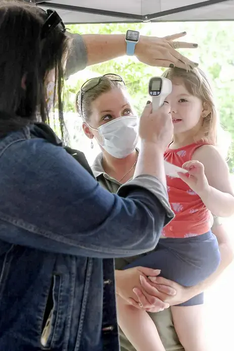 Amy Waddell holds her daughter, Aliza, 3, as her temperature is checked before spending the day at Montmorenci United Methodist Church’s day care in Candler on June 23. Image by Angela Wilhelm/Asheville Citizen Times/North Carolina News Collaborative. United States, 2020.</p>
<p>